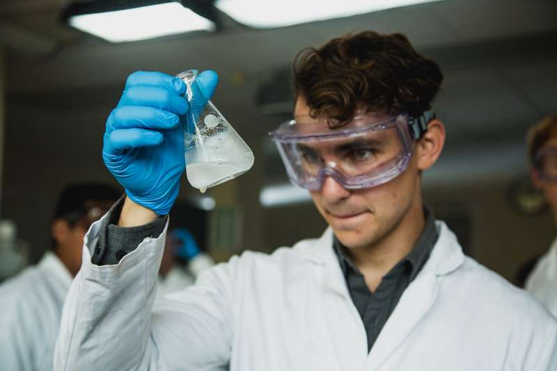 Student in a lab coat examining a beaker