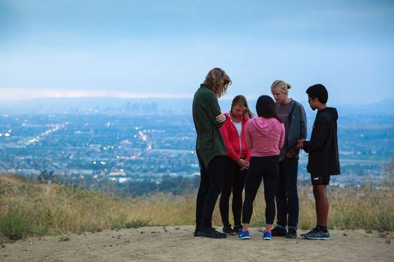 Students praying on top of a mountain, with city skyline behind them